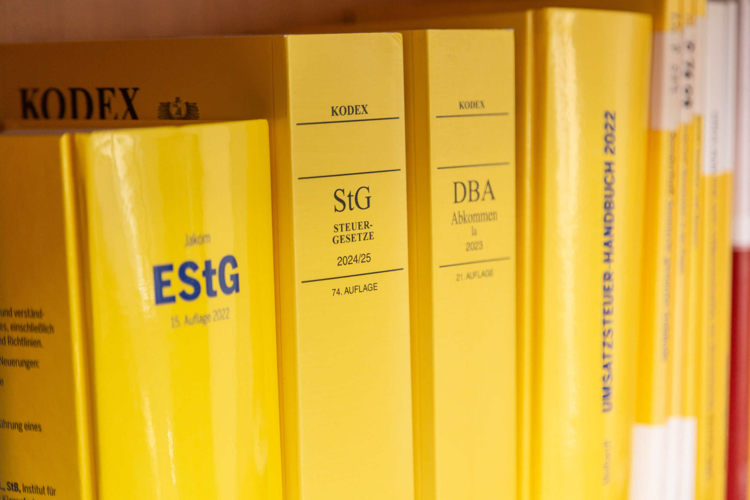Das Leistungsangebot der Steuerberatungskanzlei. Büchercover von Steuergesetz-Sammlungen: Drei gebundene Fachbücher mit den Titeln 'KODEX EStG' (Einkommensteuergesetz, Ausgabe 15. Juli 2022), 'KODEX STEUER-GESETZE 2024/25' (74. Auflage) und 'KODEX DBA Abkommen 2023' (21. Auflage). Daneben liegt das 'UNSATZ STEUER-HANDBUCH 2022'. Alle Bücher haben blaue/schwarze Einbände mit goldener Schrift.