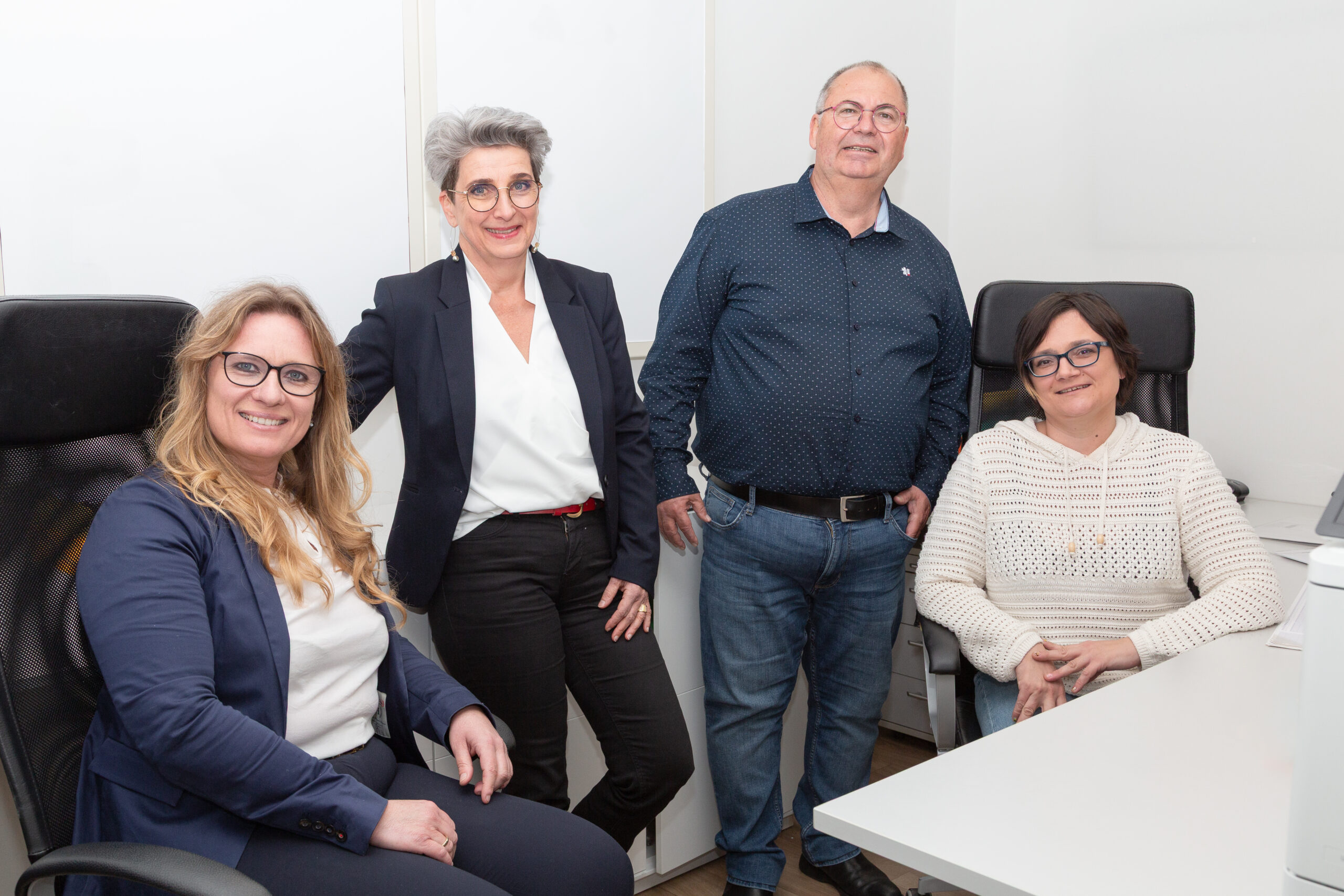 Ihre vertrauenswürdige Steuerberatungskanzlei in der Steiermark. Auf dem Foto sehen Sie das Team der Steuerberatungskanzlei. Bilanzbuchhalterin sitzend und in die Kamera lächelnd (Links), Sekretärin an der Wand angelehnt mit einem freundlichen Lächeln (Links Mitte), Steuerberater freundlich und professionell lächelnd (Rechts Mitte,) Bilanzbuchhalterin lächelnd und sitzend (Rechts)