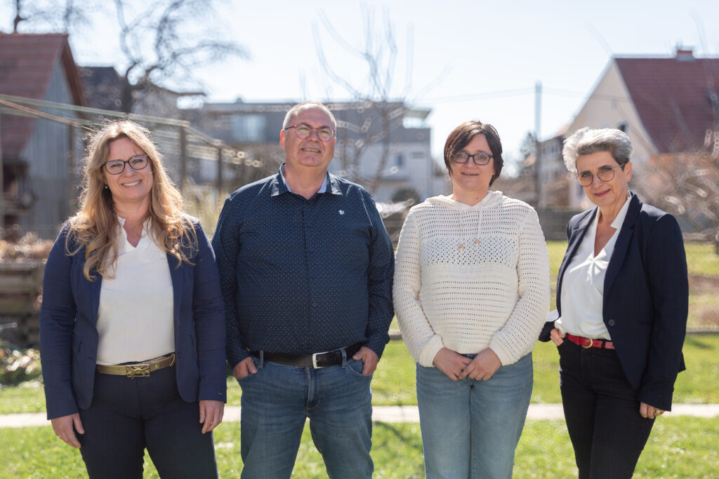Vier Angestellte der Steuerberatungskanzlei stehen lächelnd im Garten, einladend zu einem Erstgespräch: links Buchhalterin, daneben der Steuerberater, gefolgt von einer weiteren Buchhalterin und rechts die Sekretärin – alle wirken freundlich und offen.