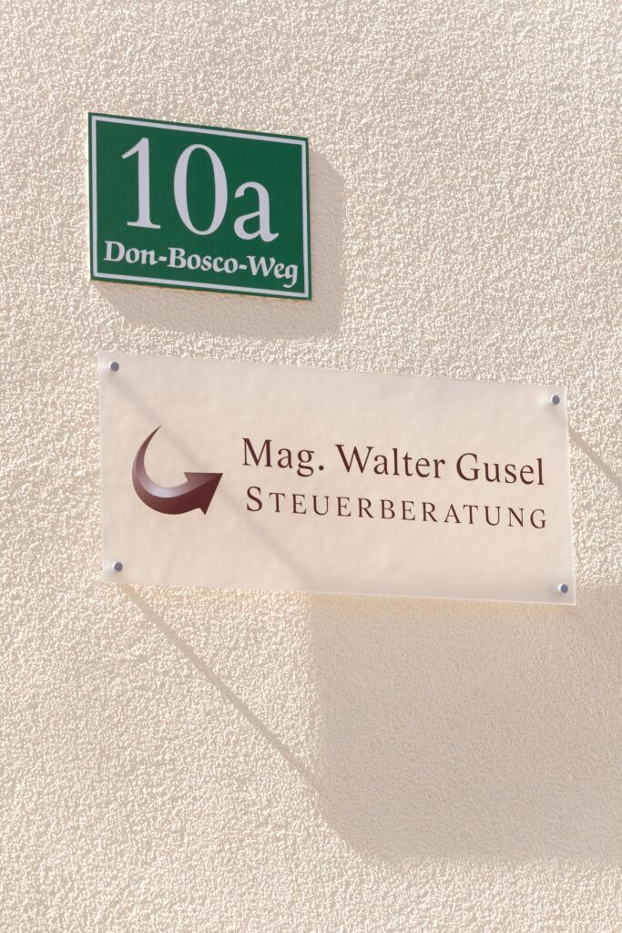 Hier sieht man die Hausnummer 10a der Steuerberatungskanzlei, mit einem Schild "Mag. Walter Gusel Steuerberatung" darunter. Die Schilder sind an einer gelben Hausfassade angebracht. 